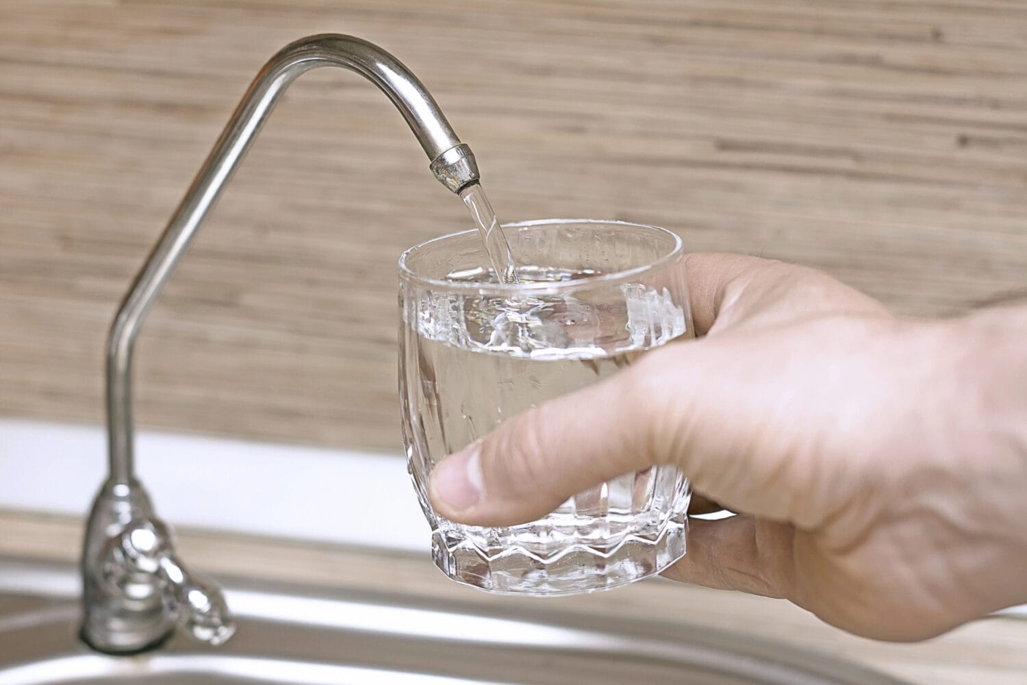 A hand holding a glass as it is filled with reverse osmosis filtered water in a kitchen sink.