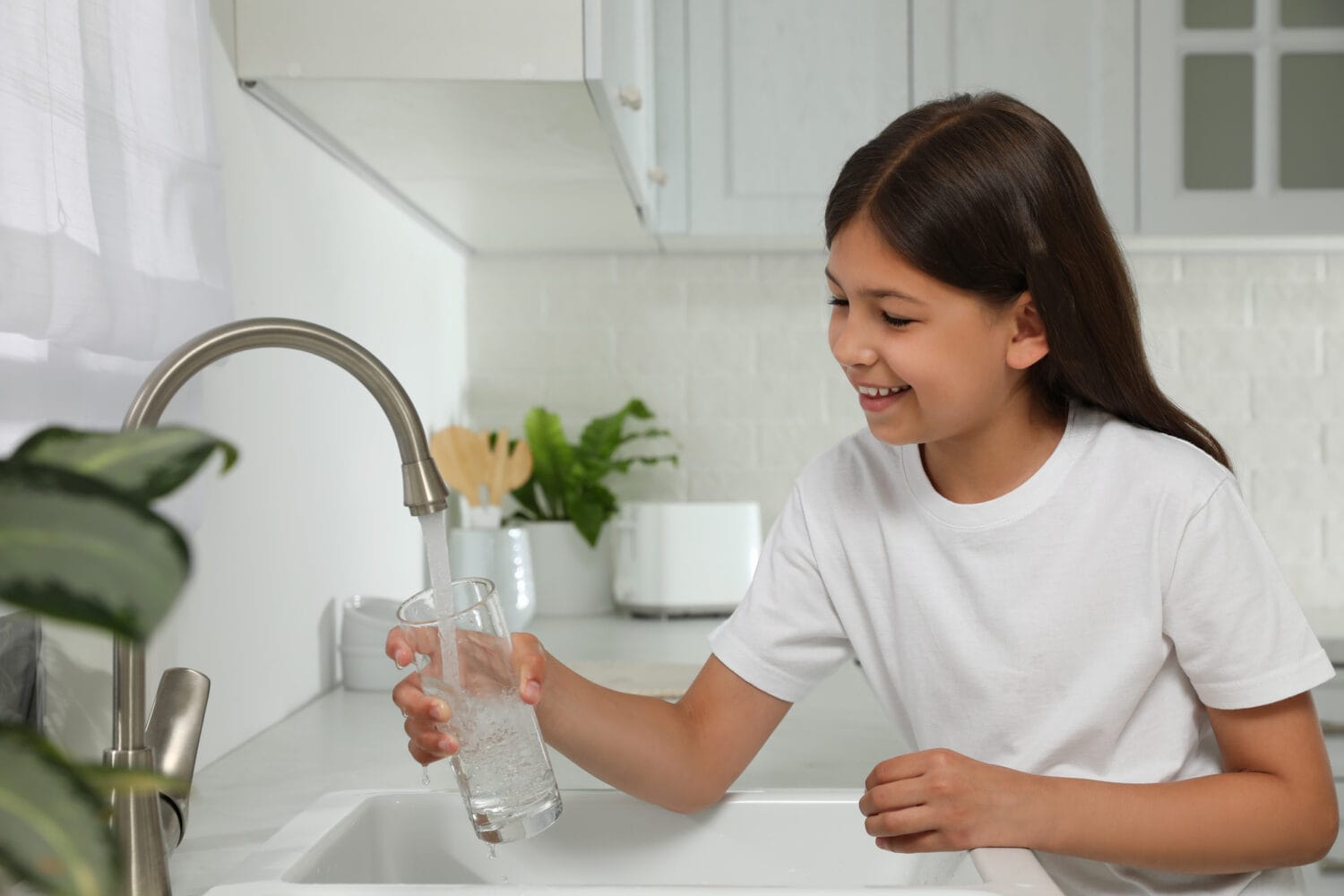 A smiling girl filling a clear glass with kitchen tap water.